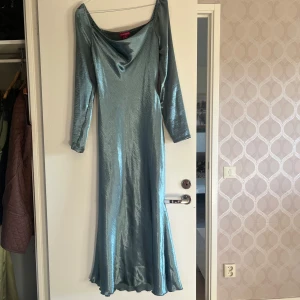 Ljusblå långklänning i satin - Säljer en elegant ljusblå klänning i satin. Klänningen har långa ärmar och en vacker draperad halsringning som ger en lyxig känsla. Perfekt för festliga tillfällen eller en speciell kväll. Klänningen har en fantastisk passform.