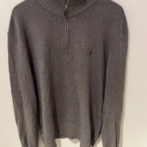 Ralph Lauren Tröja  - Jättefin grå stickad halv zip tröja från Polo Ralph Lauren. Tröjan är i okej skick och allt är dunder med den förutom lite småhål på kragen (bild 5) Tröjan är i storlek L. Tveka inte att höra av vid frågor eller funderingar!! 