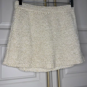 Beige stickad kjol från H&M - Mysig beige stickad kjol från H&M. Kjolen har en kort längd och en elastisk midja för bekväm passform. Perfekt för kyligare dagar med sin mjuka och varma textur.