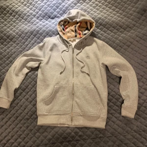 Burberry zip hoodie - Säljer en stilren grå hoodie från Burberry. Tröjan är i bra skick och inga slitningar eller hål. Perfekt för en avslappnad och trendig look.