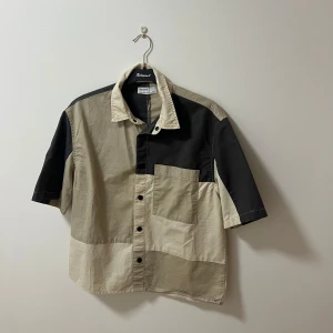 Bershka skjorta - Snygg kortärmad skjorta från Beams i beige och svart med patchwork-design. Skjortan har knappar framtill och en bröstficka. Perfekt för en avslappnad stil.