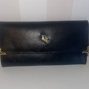 Vintage  plånbok från Christian Dior - Elegant blå plånbok i skinn från Christian Dior med guldfärgade detaljer. Plånboken har flera fack för kort och en stilren design med logotypen i guld på framsidan. Perfekt för att hålla ordning på dina kort och kontanter med stil.