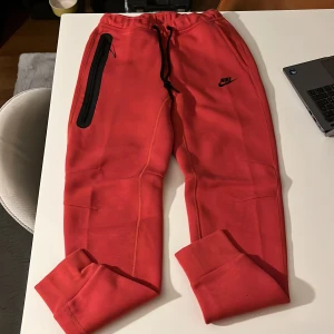 Nike tech fleece byxor - Snygga röda mjukisbyxor från Nike. Smalare modell. Perfekta för en avslappnad stil. Byxorna har en elastisk midja och är tillverkade i ett mjukt material för extra komfort. 