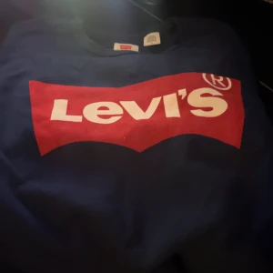 Blå tröja från Levi's - Snygg blå tröja från Levi's med det klassiska röda och vita logotyptrycket på framsidan. Perfekt för en avslappnad stil.