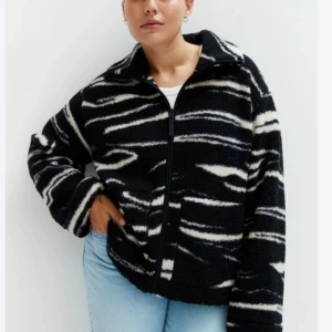 teddyjacka - Snygg och mysig svart och vit teddyjacka med ett unikt mönster. Jackan har dragkedja och långa ärmar, perfekt för kyliga dagar. Den är både stilren och bekväm, ett måste i garderoben!