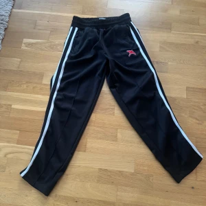 Svarta träningsbyxor från Axel Arigato - Säljer ett par svarta träningsbyxor från Axel Arigato med vita ränder längs sidorna och en röd logga. Byxorna har elastisk midja för extra komfort. Byxorna är i storlek S och i bra skick. Säljes då om inte passar längre. Jag är 174 cm lång och dom är lite korta enligt mig :)