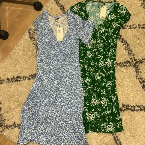 Blommiga klänningar från Indiska - Två vackra blommiga klänningar från Indiska i storlek XS. Den ena är blå med vita blommor och den andra är grön med vita blommor. Båda har en v-ringad design och korta ärmar, perfekta för sommarens varma dagar. Aldrig använda! Måste inte köpas tillsammans!! 200kr/klänning. 300kr tillsammans.