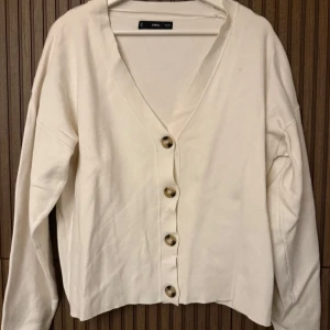 Vit kofta från MNG - Säljer en stilren vit kofta från MNG med knappar framtill. Koftan har en v-ringad design och långa ärmar, perfekt för en elegant och avslappnad look.