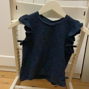 Mörkblå topp  - Säljer en söt mörkblå topp från Lindex Kids. Toppen har volangdetaljer vid ärmarna och en fin textur i tyget. Vågigt mönster 