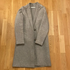 Grå kappa från Zara - Snygg grå kappa från Zara Trafaluc med klassisk design och knappar framtill. Perfekt för kyligare dagar med sin stilrena look och långa ärmar. Ett måste i garderoben för en chic och tidlös stil.