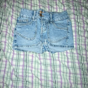 Blå jeansshorts med broderi - Snygga blå jeansshorts med hög midja (kan justeras) och dekorativa broderier på bakfickorna. Shortsen har en klassisk femficksdesign och stängs med dragkedja och knapp framtill. Perfekta för sommardagar!