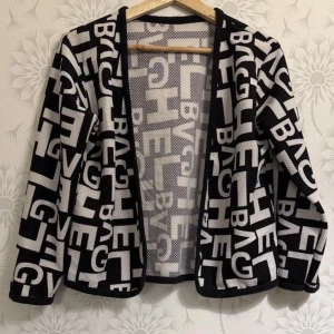 Svart och vit mönstrad jacka - Snygg svart och vit jacka med ett iögonfallande bokstavsmönster. Jackan har långa ärmar och en öppen design utan knappar eller dragkedja. Perfekt för att ge en cool touch till din outfit.i ny skick 