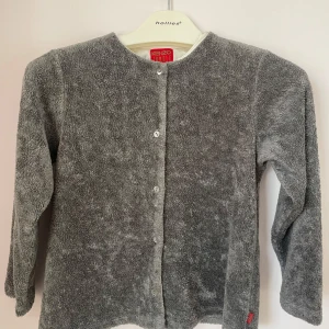 Grå kofta från Kenzo Jungle för junior storlek 10 - Junior storlek 10. Mysig grå kofta från Kenzo Jungle med knappar framtill. Baksidan har en vacker broderad detalj med blommor och blad i vitt och gult, inramad av ett rött mönster. Perfekt för att hålla sig varm.