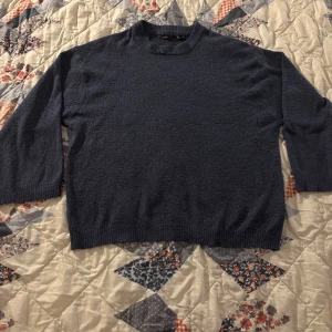 Mörkblå stickad tröja - Säljer en mörkblå stickad tröja med trekvartsärm. Perfekt för kyliga dagar och har en klassisk rund halsringning. Tröjan är enkel och stilren, vilket gör den lätt att matcha med olika outfits.