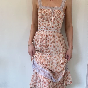 Blommig klänning med spetsdetaljer - Charmig blommig klänning i ljusa toner med spetsdetaljer vid axelband och byst. Urban outfitters