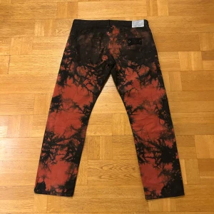 Mönstrade byxor från Stone Island - Unika byxor från Stone Island med ett coolt mönster i svart och röd. Byxorna har en normal passform och är tillverkade i ett slitstarkt material. Perfekta för dig som vill sticka ut med en edgy stil.