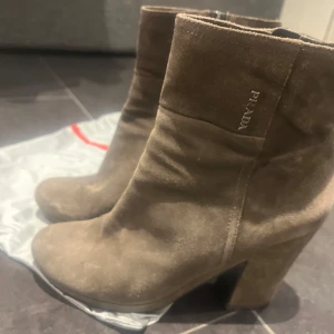 Bruna mocka boots från Prada - Snygga bruna mocka boots från Prada med klack. Perfekta för höst och vinter. Stilren design med diskret logotyp på sidan.
