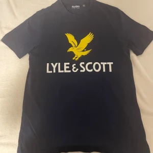 Marinblå t-shirt från Lyle & Scott - Snygg marinblå t-shirt från Lyle & Scott med deras ikoniska gula örn och vit logotyp på bröstet. Perfekt för en avslappnad stil.