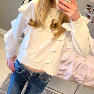 Vit tröja med volangdetaljer från IVYREVEL 💕 - Säljer en stilren vit tröja från Ivyrevel med snygga volangdetaljer längs ärmarna. Tröjan har en rund halsringning och långa ärmar. Tröjan används inte och därav säljer jag den, lite nopprig men de tänker man inte på, står ingen storlek i men skulle uppskatta runt XS/S