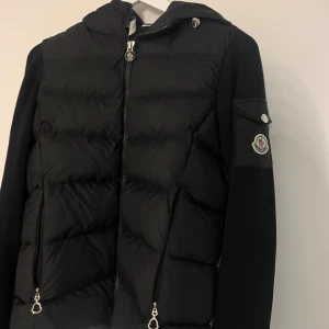 Moncler cardigan - Snygg svart dunjacka från Moncler med huva och dragkedja. Den är som ny det ända som är e att där man hänger upp jackan har gått av. Dm för fler frågor🤍