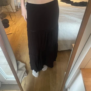 Svart långkjol - Snygg svart långkjol med en enkel och elegant design. Kjolen har en lätt rynkad detalj nedtill som ger en fin rörelse. Perfekt för en stilren look.