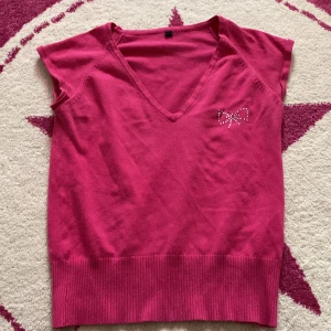 Mcbling topp - Snygg rosa topp från H&M Divided med en glittrig rosett-detalj på bröstet. Toppen har en v-ringad hals och är ärmlös, perfekt för en somrig look. Tillverkad i en mjuk bomullsblandning för extra komfort.