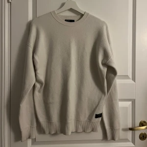 Vit tröja från Bershka - Säljer en stilren vit tröja från Bershka. Tröjan har långa ärmar och ribbade muddar vid ärmslut och nederkant. Perfekt för en minimalistisk look. Märke längst ned på framsidan med texten 'O. Drops'. 