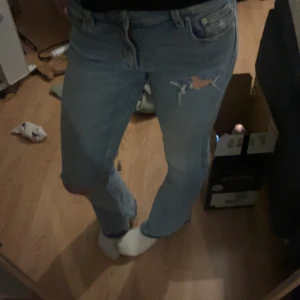 Blå jeans med slitningar - Säljer ett par blå jeans med slitningar på framsidan. De har en klassisk femficksdesign och en bekväm passform. Perfekta för en avslappnad stil.
