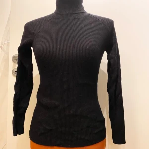 Svart ribbad polotröja Cubus S - Snygg svart ribbad polotröja med lång ärm. Perfekt för kyligare dagar och ger en stilren look. Passar bra till både jeans och kjol. Svart långärmad ribbstickad polotröja Längd: 56 cm Armhåla till armhåla: 38 cm  Inga bilder när den sitter på mig! Katter finns i hemmet Kan ej skicka med UPS!