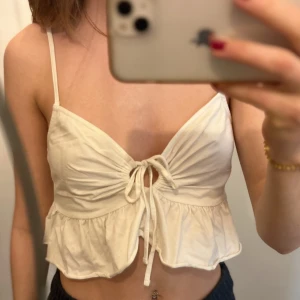 Vit ärmlös topp med volangdetaljer - Säljer en söt vit ärmlös topp med smala axelband och volangdetaljer. Köpt på NLY trend och är i storlek M. Använd en del men är trots det i bra skick.
