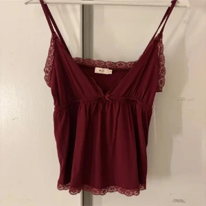 Vinröd linne med spetsdetaljer - Säljer ett vinrött linne från Nelly med v-ringning och spetsdetaljer längs kanterna. Perfekt för en stilren och bekväm look. Toppen är slutsålt från hemsidan 😊 