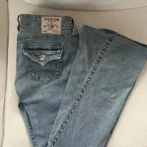 Blå jeans från True Religion - Säljer ett par snygga blå jeans från True Religion, modell Joey Low Rise Flare. De har en låg midja och en utsvängd stil. Perfekta för en avslappnad look med en touch av stil.