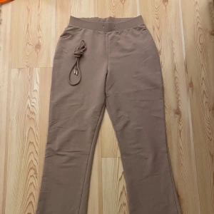 Beige byxor från NLY Trend - Säljer ett par beige byxor från NLY Trend i storlek S. Byxorna har en hög midja och är tillverkade i en mjuk bomulls- och polyesterblandning. De har en knytning i midjan för extra stil och komfort.Utsvängda nedtill!  Snöret i midjan togs ut vid tvätt med medföljer.  Inga skador eller anmärkningar.  Mycket bra skick!