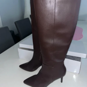 Bruna stövlar från Nelly - Aldrig använda!! Snygga bruna stövlar från Nelly med spetsig tå och klack. De är knähöga och har en dragkedja på insidan för enkel på- och avtagning. Perfekta för en stilren look. 