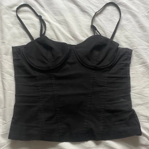 korsett topp - Snygg svart korsett topp med justerbara axelband. Toppen har en figurnära passform. Den är väl använd men det är ingenting som direkt syns! Liten i storlek, känns mer som en XXS