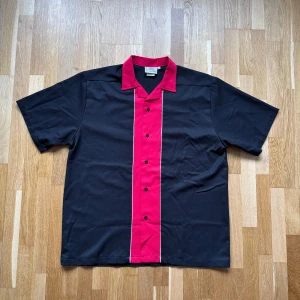 Vintage Cruisin USA Svart Bowlingskjorta - Svart Bowlingskjorta med röda och vita detaljer från Cruisin USA.  Storlek: L, Armhåla till Armhåla: 64 cm, Längd: 78 cm, Axel till Armöppning: 28.5 cm.  Material: 65% Polyester, 35% Rayon