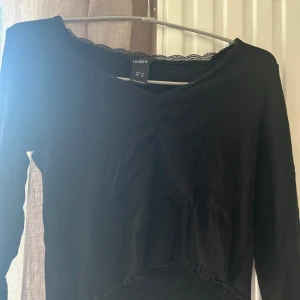 Svart långärmad topp från Lindex - Säljer en svart långärmad topp från Lindex i storlek XS. Toppen har en v-ringad hals med spetsdetaljer som ger en elegant touch. Perfekt för att matcha med olika outfits. Köparen står för frakten! Pris kan diskuteras💖