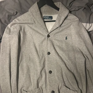 Grå Cardigan från Polo Ralph Lauren - Säljer en stilren grå Cardigan från Polo Ralph Lauren med knappar framtill och broderad logga på bröstet. Perfekt för en avslappnad men snygg look. Pris kan diskuteras i dm och fråga alltid om du undrar något. 