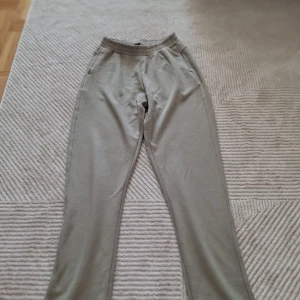 olivgröna mjukisbyxor - Säljer ett par bekväma beige mjukisbyxor med elastisk midja. Perfekta för en avslappnad dag hemma eller en snabb tur till affären. Byxorna har en enkel design utan extra detaljer.