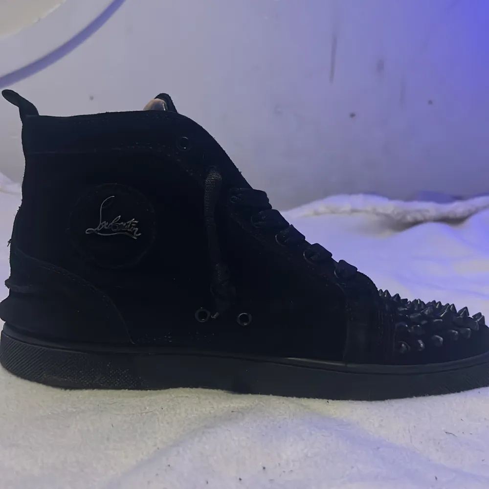 Snygga svarta sneakers med nitar på tån och en ikonisk röd sula. Skorna har snörning och är tillverkade i skinn. Perfekta för att ge en edgy touch till din stil. Storlek 43 eur. Kengät.