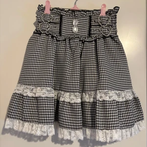 Svartvit rutig kjol med spetsdetaljer - Charmig svartvit rutig kjol med volanger och spetsdetaljer. Kjolen har dekorativa knappar och snörning i midjan för en söt look. Perfekt för dig som gillar en klassisk stil med en twist. Från det japanska märket Dear My Love - perfekt för jirai kei och ryousangata. Matchande top finns i min profil!