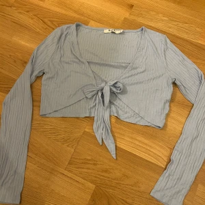 Ljusblå ribbad knytblus från NA-KD - Säljer en ljusblå ribbad blus från NA-KD med knytning framtill. Blusen har långa ärmar och en v-ringad design. 