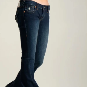 Blå Joey low rise flare- True Religion  - Snygga mörkblå flare jeans från True Religion med ikoniska bakfickor och kontrastsömmar.  Jeansen är i väldigt bra skick. Då de bara är använda två gånger. Köpta i butik för 1 299kr.