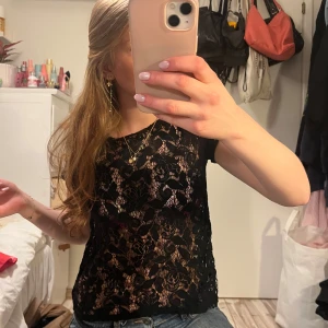 Svart spetsblus - Säljer en elegant svart spetsblus med korta ärmar. Perfekt för en stilren look med ett vackert spetsmönster som ger en feminin touch. Passar bra till både jeans och kjol. Trendig! 