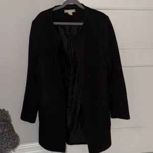 Svart kappa från H&M - Snygg svart kappa med lång ärm och stilren design. Perfekt för hösten eller vår. Den har en enkel och elegant look utan krage. Passar bra till både vardag och mer uppklädda tillfällen🤗🖤