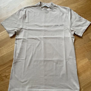 Samsøe Norsbro T-shirt - Farligt snygg T-shirt från samsøe samsøe i storlek medium, som är oerhört taggad på ny ägare. Beige och runt 700kr nypris. Är inte särskilt använd och har mest legat och samlat på sig damm i garderoben. Är du sugen så är den inte enklare än att dra i väg ett meddelande!