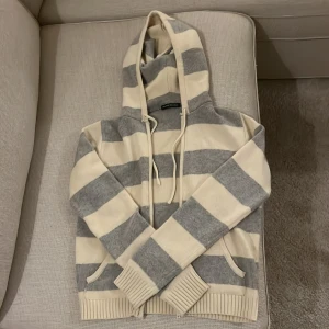 Randig hoodie från Brandy Melville - Säljer en mysig randig hoodie från Brandy Melville i grått och beige. Den har en klassisk huva med dragsko och ribbade muddar vid ärmslut och nederkant. Perfekt för en avslappnad stil. Storleken är one size❤️