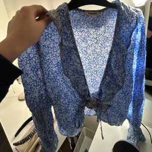 Ljusblå blus med blom detaljer och ett knyttsnörre   - Jätte fin till sommaren när man ska åka till stranden eller jätte fin på våren när det börjar bli blomstring utomhus!