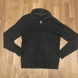 Mörkgrå tröja med dragkedja från Jack & Jones - Snygg mörkgrå tröja från Jack & Jones med dragkedja vid halsen. Perfekt för en stilren look. Tröjan har långa ärmar och en bekväm passform.