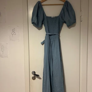 Himmelsblå klänning från & Other Stories - Himmelsblå klänning från & Other Stories med puffiga kortärmar och smockdetaljer. Klänningen har en knytning i midjan för en fin passform! Inköpt för ca 1200 kr. 